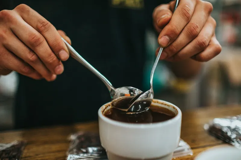 Two spoons held over a coffee cupping bowl