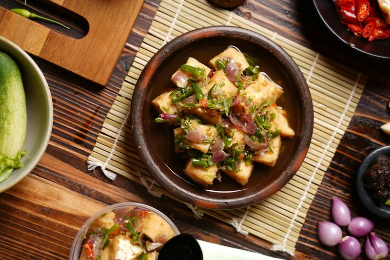 A bowl of fried tofu on a bamboo mat with vegetables around it